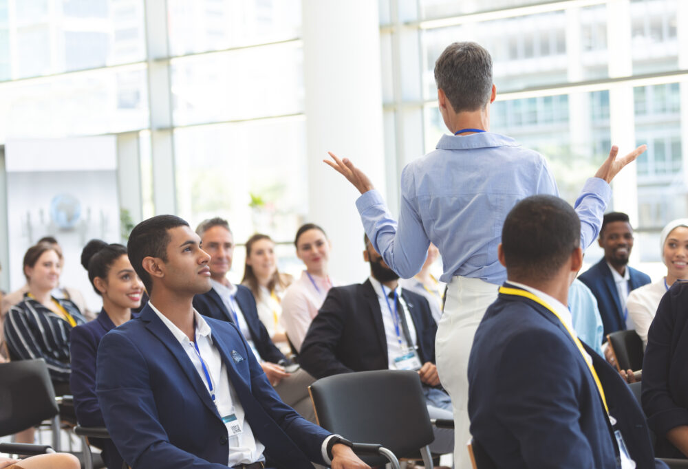 Rear view of mature caucasian businesswoman asking question to diverse business people during seminar in office building